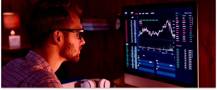 A man in glasses studies stock market information on a computer, illustrating the role of a forex broker.