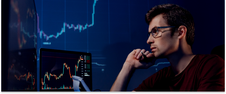 A man in glasses analyzes stock market graphs on a screen, representing his work as a forex broker.
