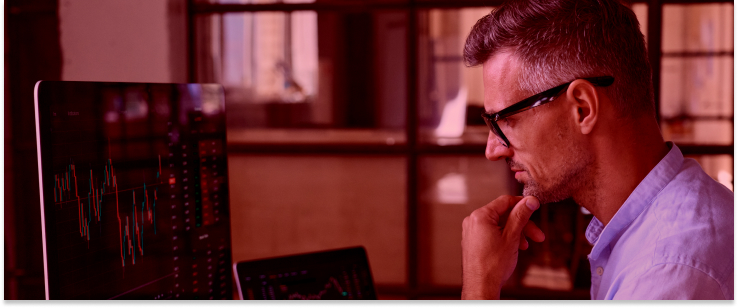 A man wearing glasses intently observes a computer screen, focused on his work as a forex trader.
