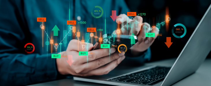 Man analyzing stock market graphs on a laptop while using a smartphone for additional data.