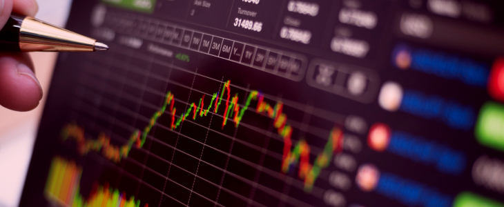 An individual uses a pen to annotate a screen featuring a stock market graph, focusing on market trends.